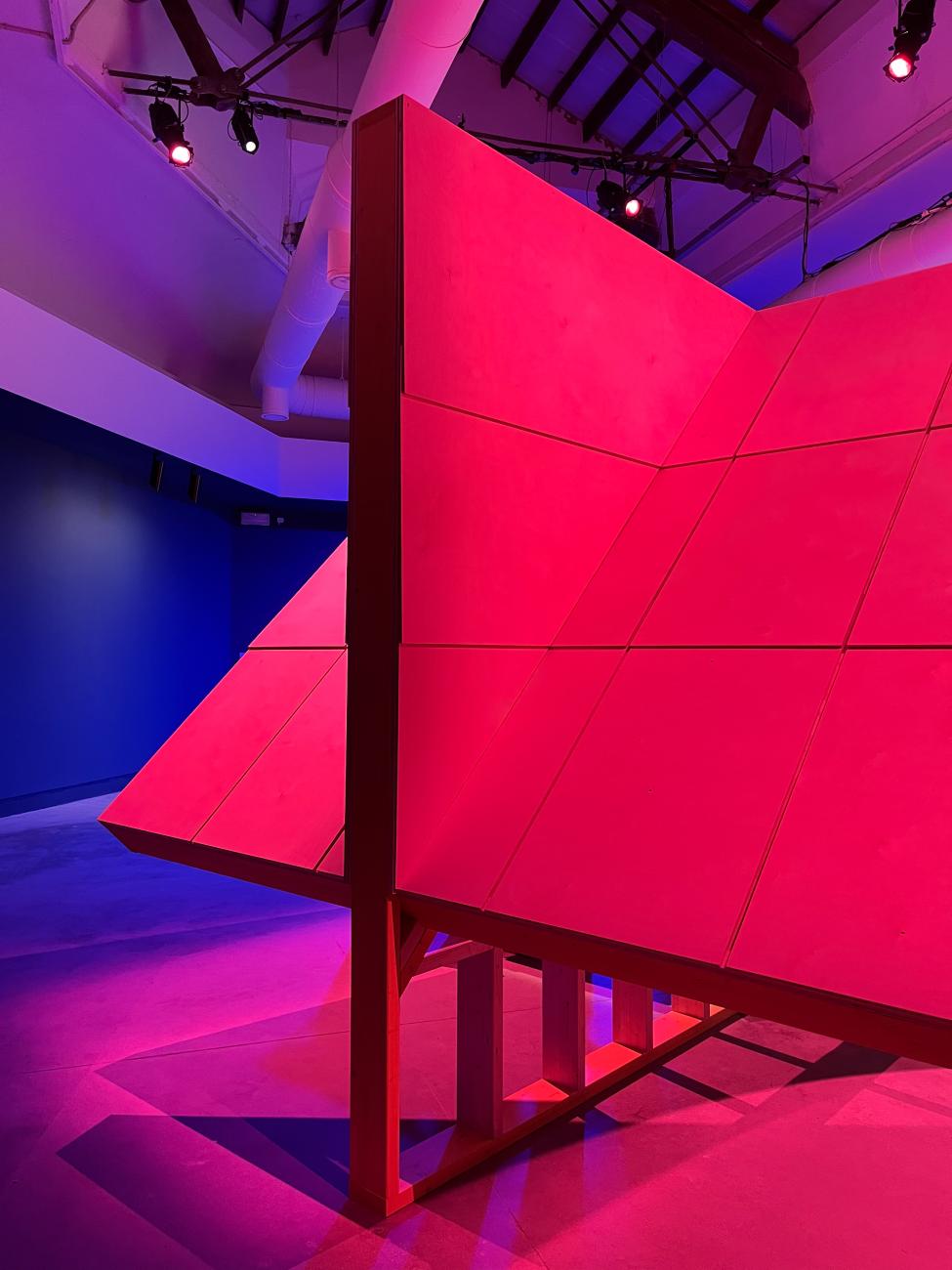 Steep pitched roof structure in an interior space with purple and magenta lighting