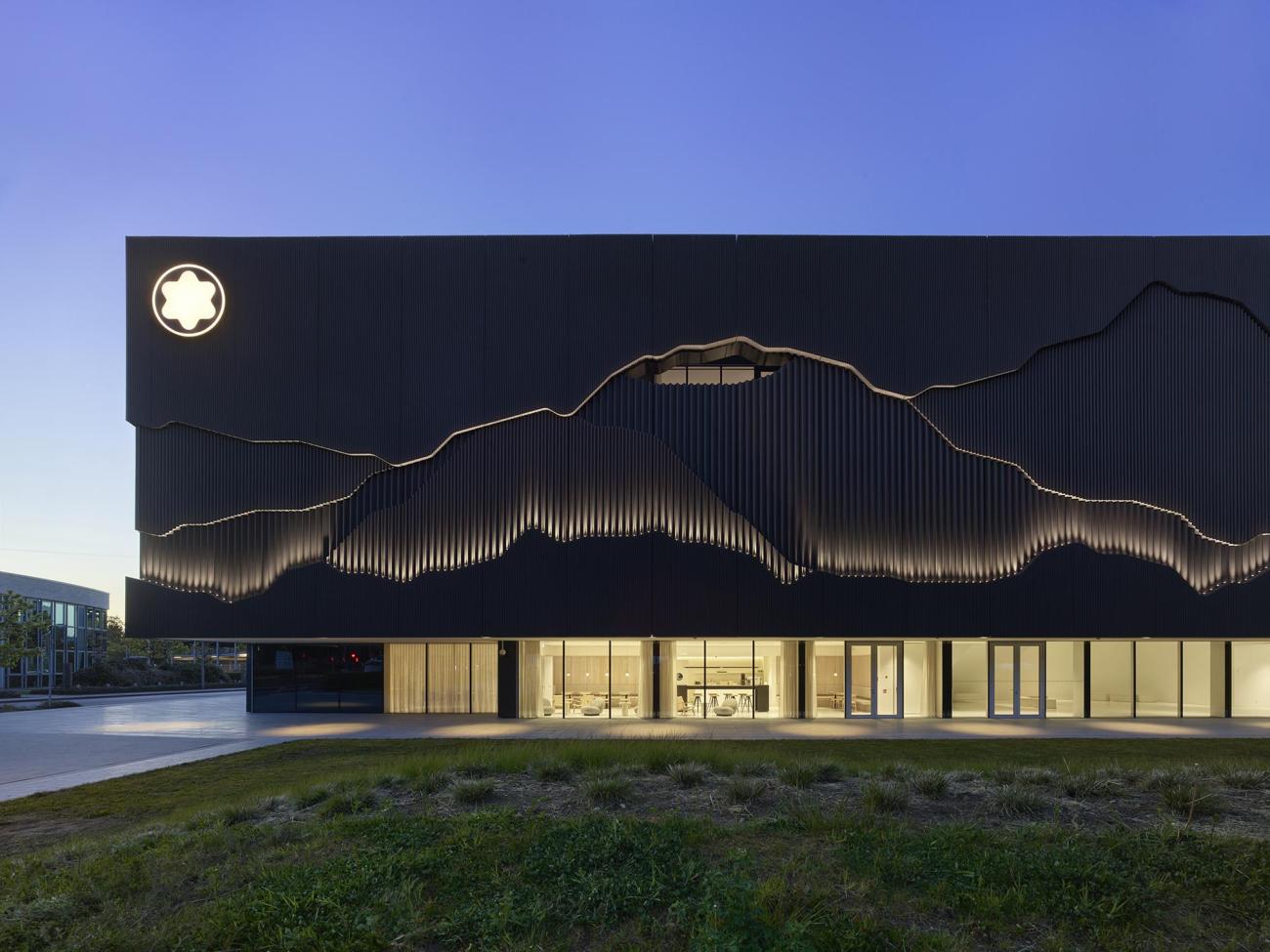 A rectangular black building with a ribbon of windows on the lower level and a geometric form in relief on the facade