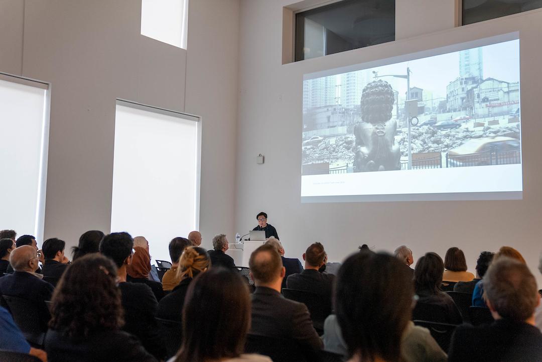 Image of man standing at a lecturn speaking to a small crowd