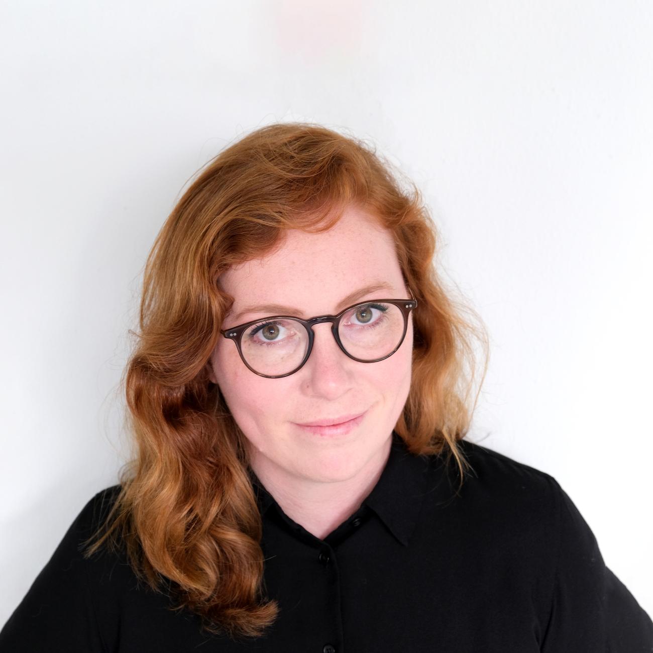 Image of a red-headed woman wearing wire rimmed glasses and a blue shirt